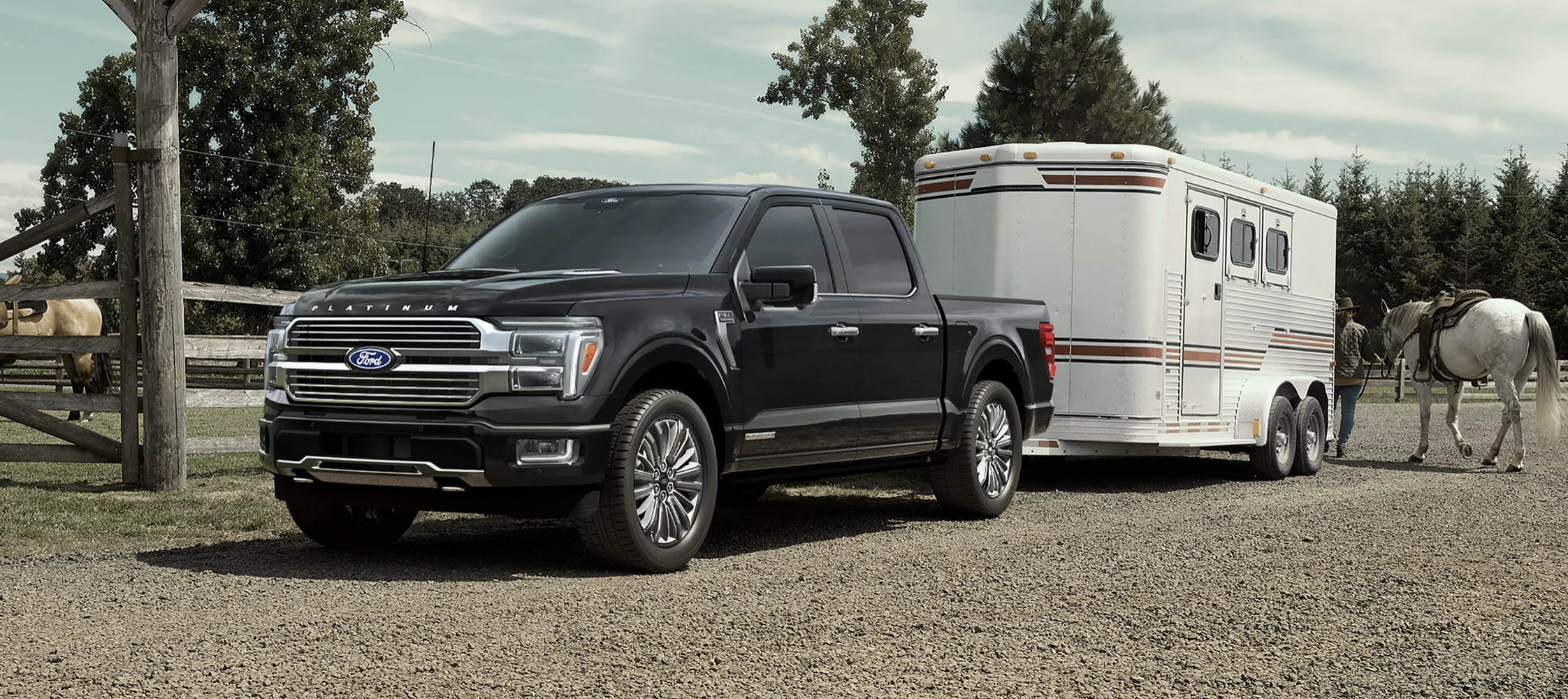 A black Ford F-150 with a hitched trailer on a dirt road on a ranch.