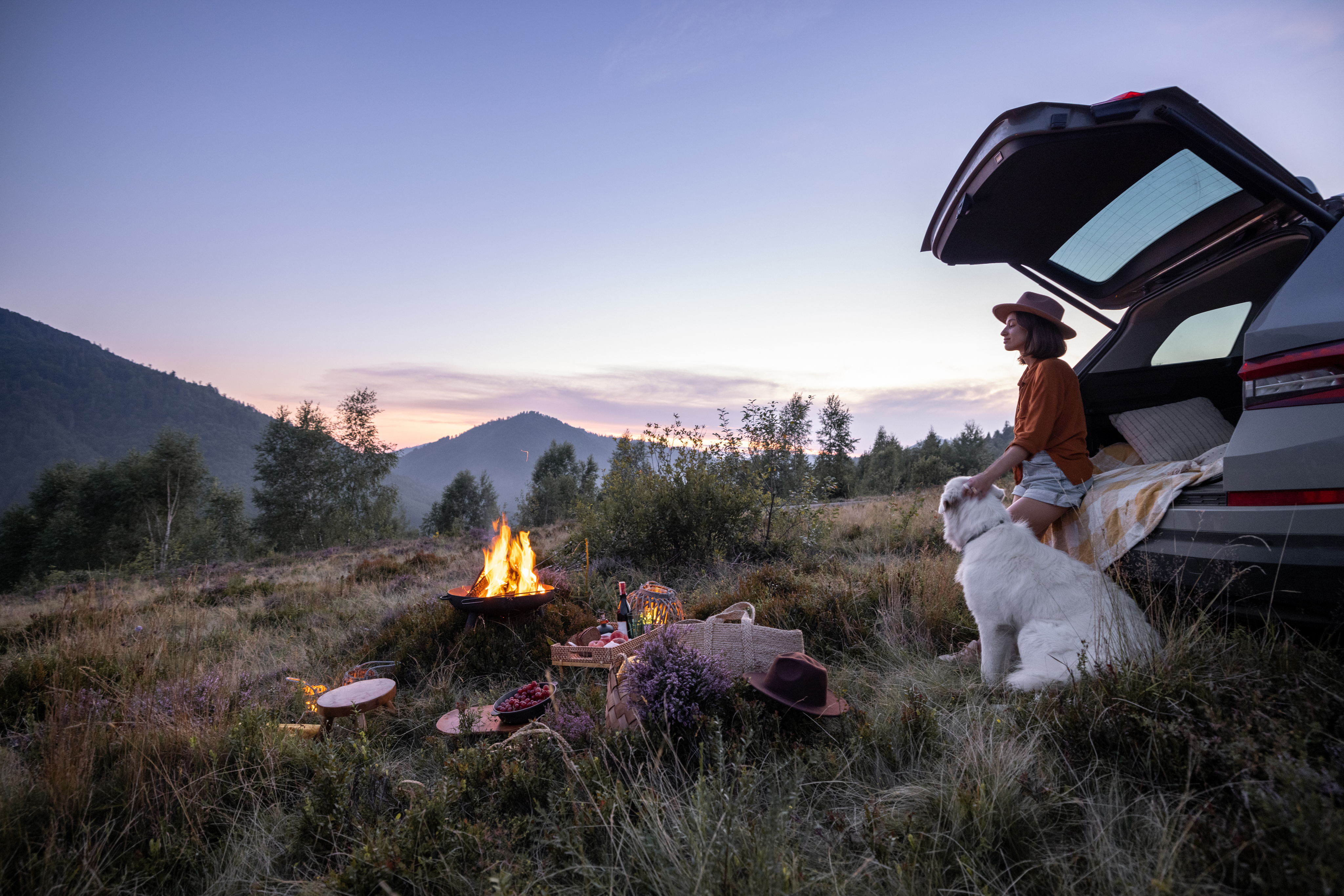 A woman camping out of her car with her dog on the plains
